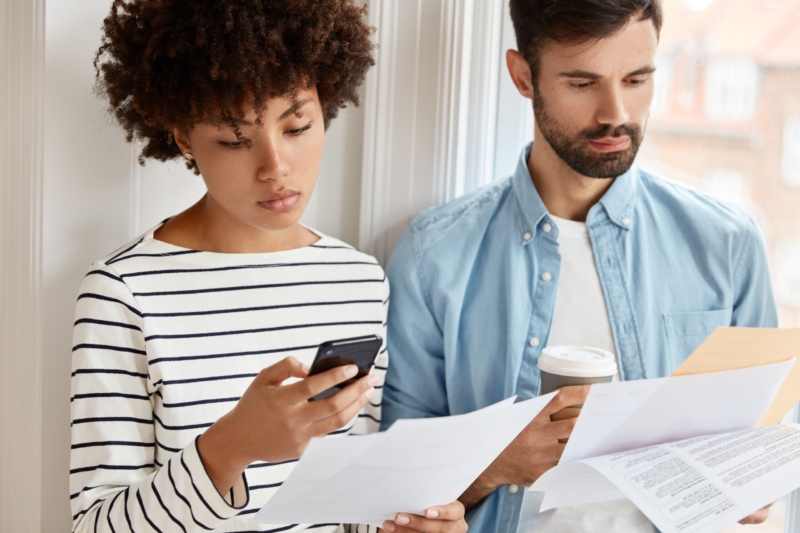 Cropped shot of interracial colleagues discuss statistics financial options, hold paper documents, African American woman makes accounting on cell phone, bearded guy in shirt drinks takeaway coffee